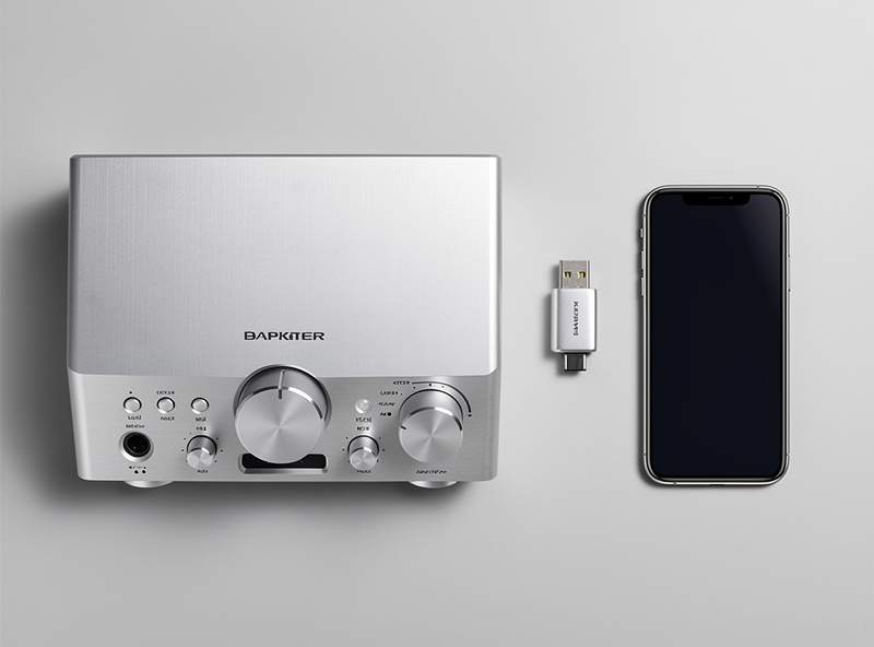 A desktop DAC with display and volume knob beside a small USB-C portable DAC dongle and a phone